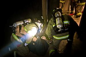Photo from Cadet Fire Exam-two students in fire bunker gear performing rescue of man in simulated burning building 
